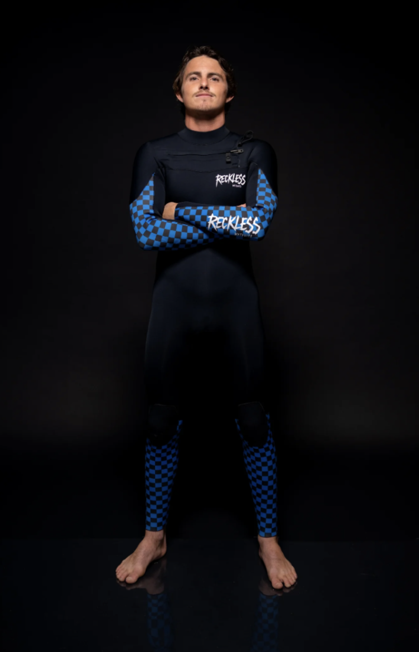 Rider in a Reckless chest-zip steamer with checkerboard arm and shin panels, studio, black ground