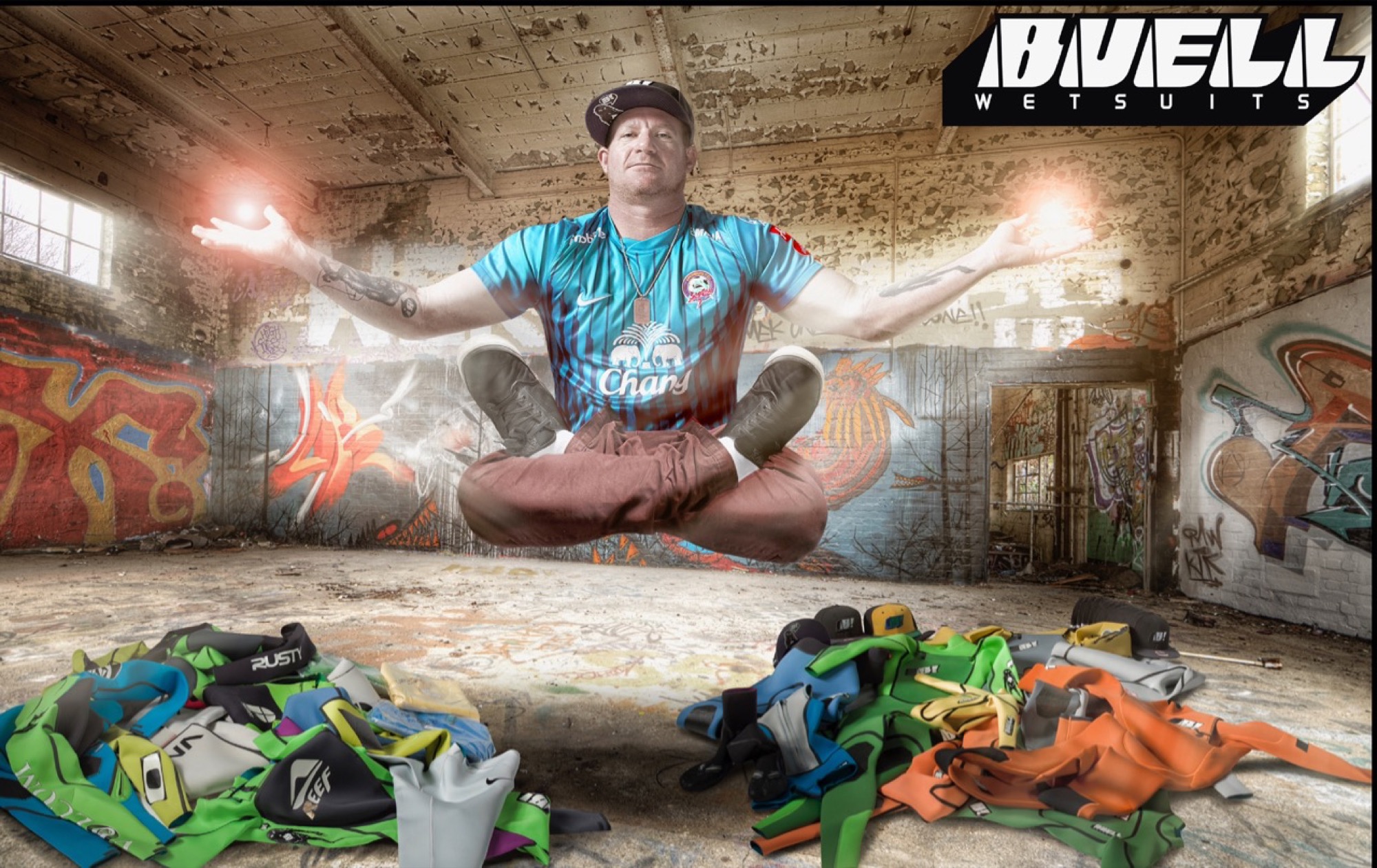 Ryan Buell seated above a floor covered in wetsuits from every brand he has designed for